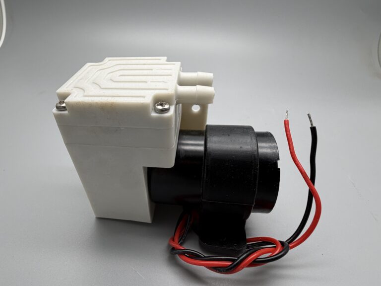 Miniature pump with a white pump head, two hose ports and molded flow-direction arrows
